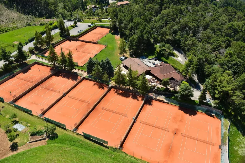 Vista aerea campi da tennis rossi e vegetazione.