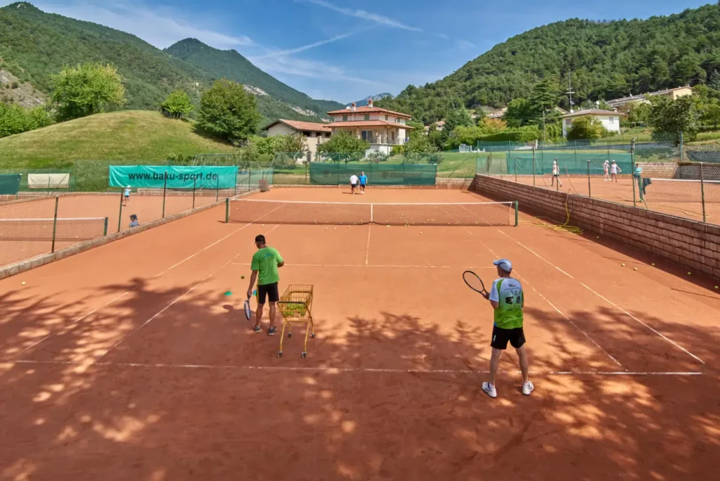 Campo da tennis all'aperto con giocatori e montagne.