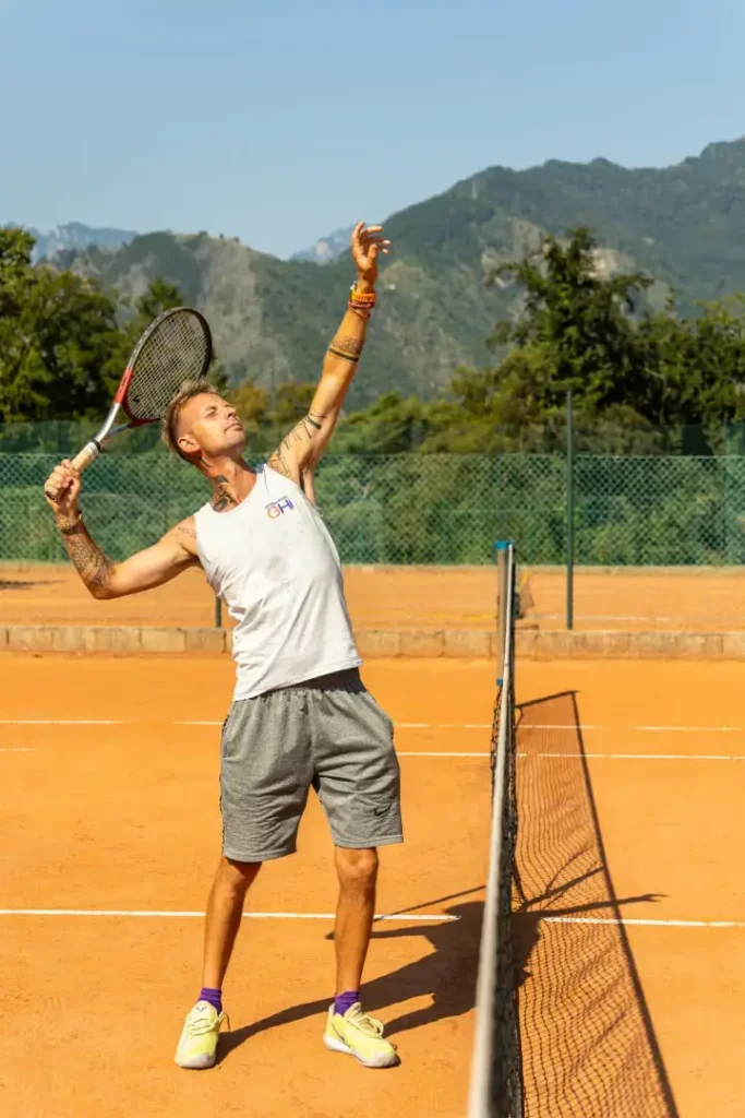 Giocatore di tennis serve su campo in terra.