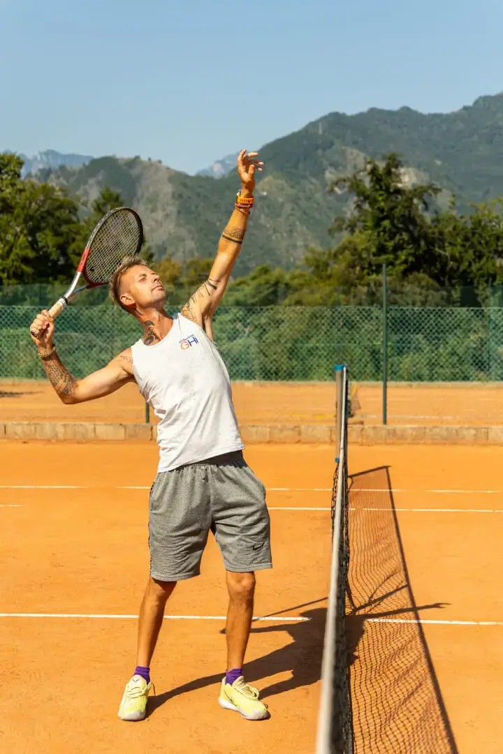 Giocatore di tennis serve su campo in terra.
